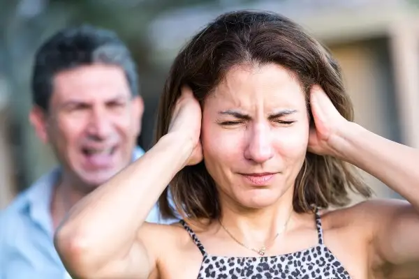 A woman covering her ears while a man shouts behind her