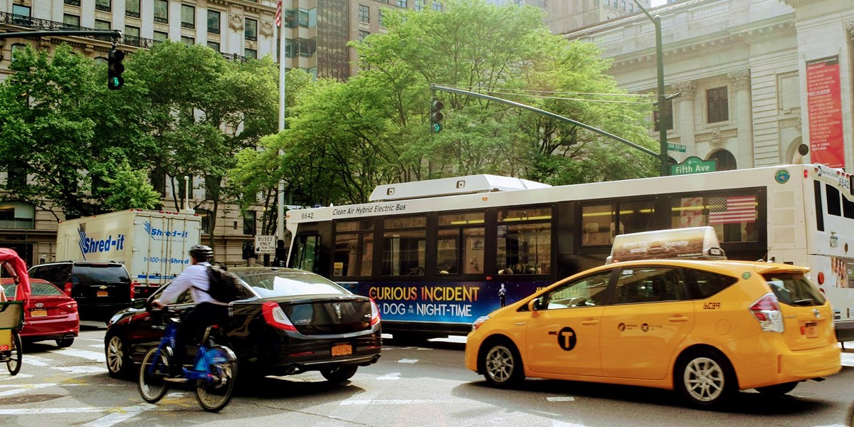 A cyclist, a bus and a taxi at a busy city intersection