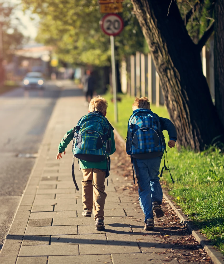 Two children with backpacks walking home along a pavement
