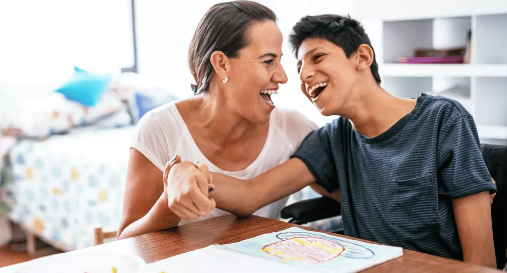 A carer and a young person in a wheelchair laughing together